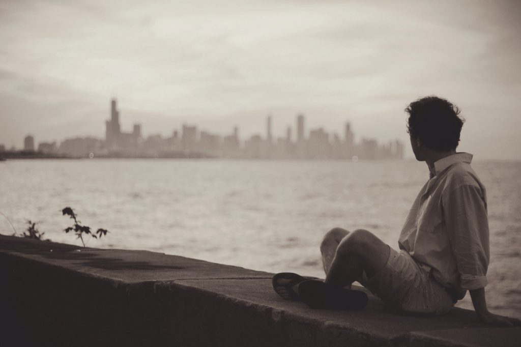 Man sitting on ocean wall looking at the city
